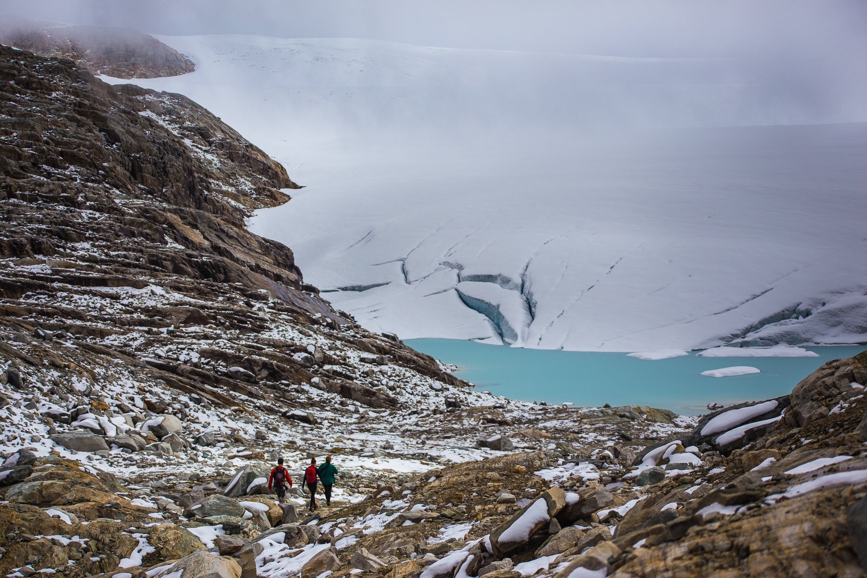 Three people hiking down to a glacier