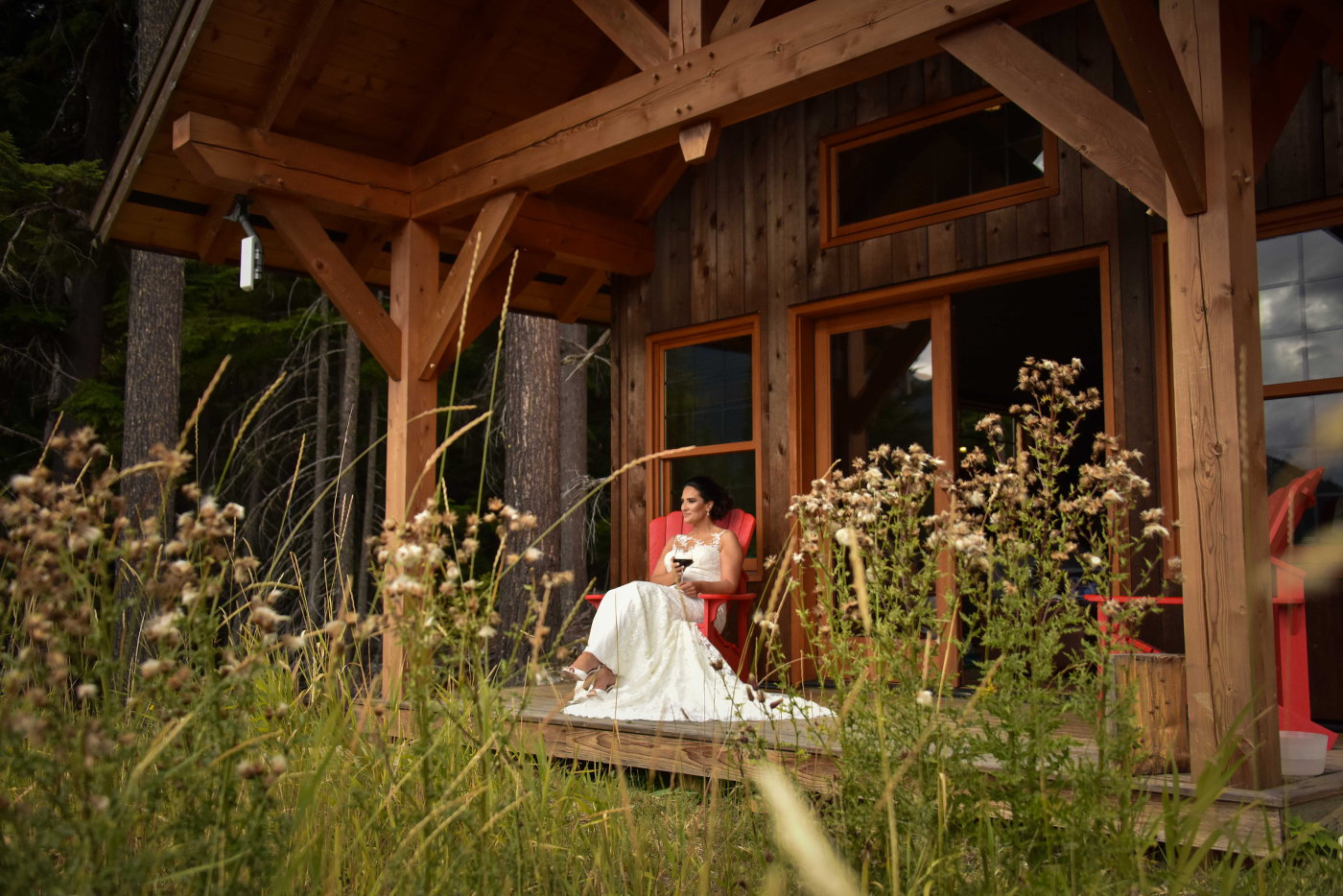 Happy bride relaxing in a chair against a cabin with a glass of wine